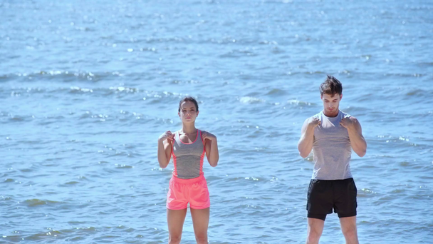 jonge man en vrouw in sportkleding die samen sporten op het strand  - Video