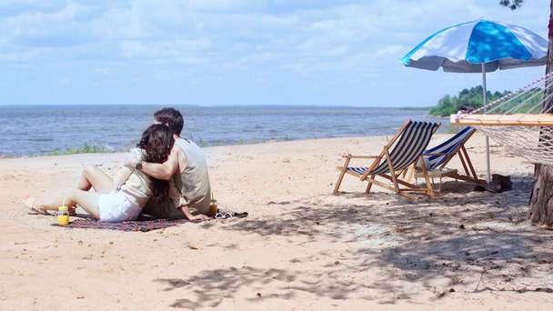 nuori pari syleilee ja puhuu istuessaan hiekkarannalla
 - Materiaali, video