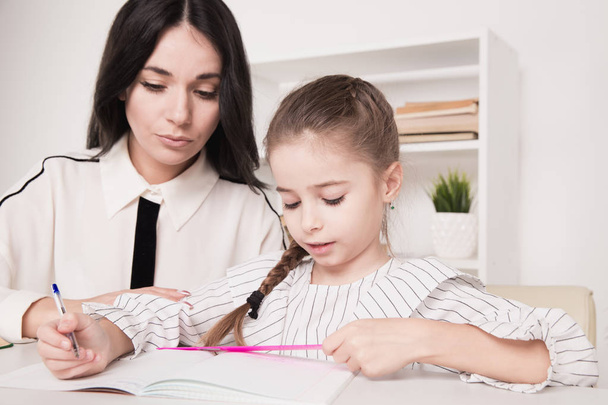 Pretty family concept. Mom and daughter sitting together and studying at home. - Foto, imagen