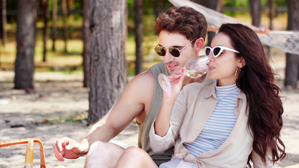 幸せな若者がガールフレンドを抱きしめ、髪の毛に触れ、ビーチで休んでいる間にグラスに白ワインを注ぐ - 映像、動画