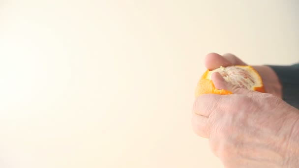 Older man removes the peel from an orange. - Imágenes, Vídeo