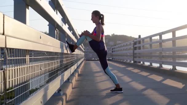 Sports woman stretching her legs before run. Young woman doing morning exercises on pier - Video, Çekim