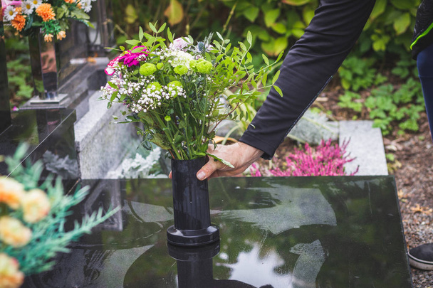 Man zet boeket bloemen op grafsteen op begraafplaats. Verdriet voor dode persoon op alle zielen dag. Bloemstuk op tombstone - Foto, afbeelding