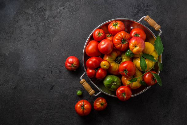 Ripe tomatoes in a pan on black stone background, copy space - Photo, Image