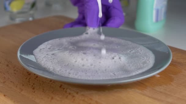 A hand in blue protective gloves squeezes a yellow-green sponge. The foam bubbles and drains onto a gray plate. Slow motion. Housekeeping with quality detergent - Footage, Video