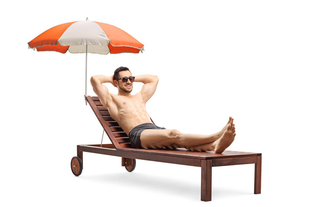 Young man lying on a sunbed under umbrella - Fotó, kép