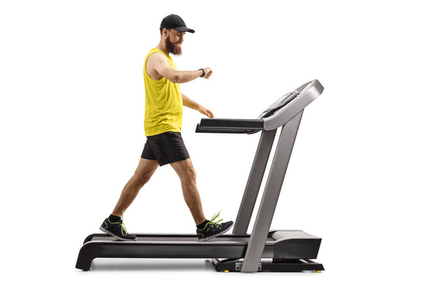 Bearded man walking on a treadmill and looking at his smartwatch - Foto, Imagem