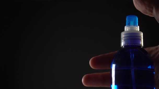 De hand drukt op de knop van de blauwe spray en de spray vliegt voorwaarts onder druk op een zwarte achtergrond - Video