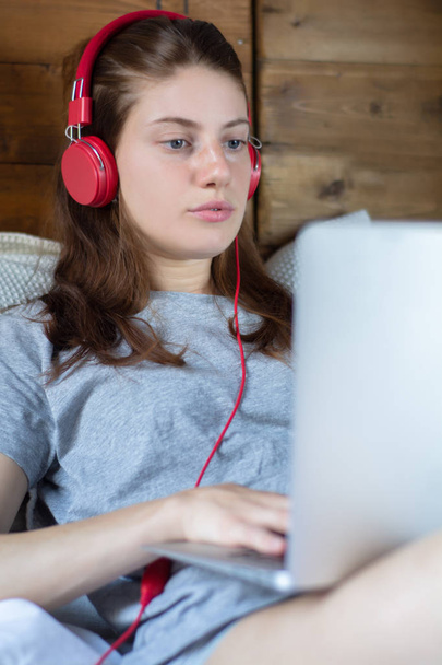 Молода жінка використовує ноутбук і навушники в ліжку
. - Фото, зображення