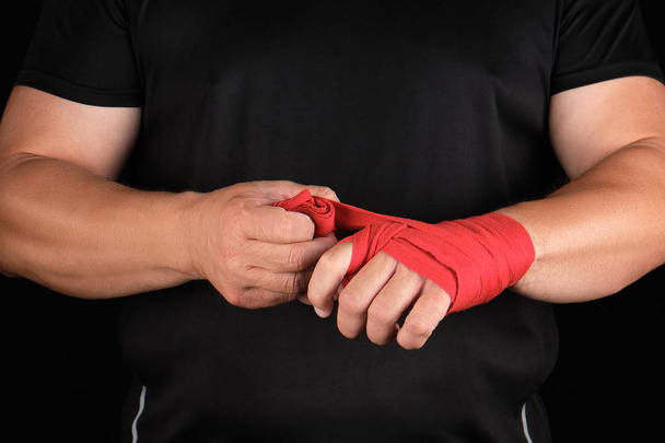 athlete stand in black clothes and wrap his hands in red textile - Фото, изображение