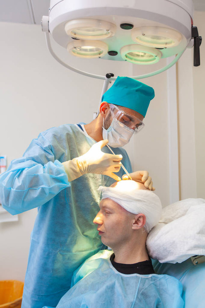 The surgeon gives injections to the head. Baldness treatment. Hair transplant. Surgeons in the operating room carry out hair transplant surgery. Surgical technique that moves hair follicles from a - 写真・画像