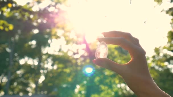 Frauenhand mit transparentem Amethyst-Quarz-Yoni-Ei für Vumfit, Imbuilding oder Meditation. leuchtende Kristall-Ei in den Händen am Himmel und Sonnenaufgang Hintergrund im Freien. Frauengesundheitskonzept. - Filmmaterial, Video