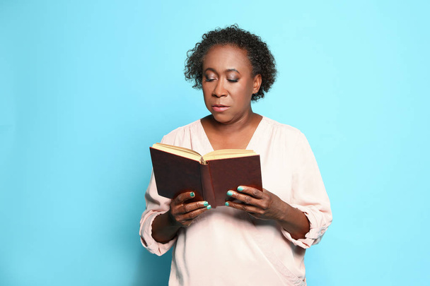 Portrait of mature African-American woman reading book on light blue background - Φωτογραφία, εικόνα
