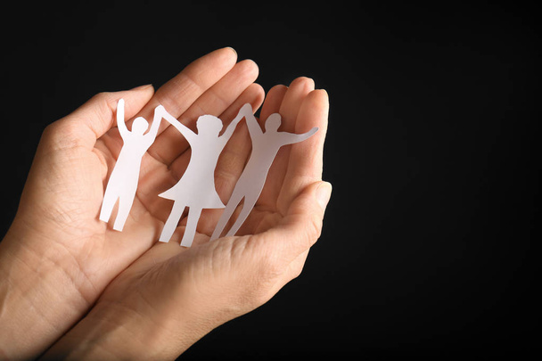 Mujer sosteniendo la silueta de papel de la familia en las manos sobre fondo negro, primer plano. Espacio para texto
 - Foto, Imagen