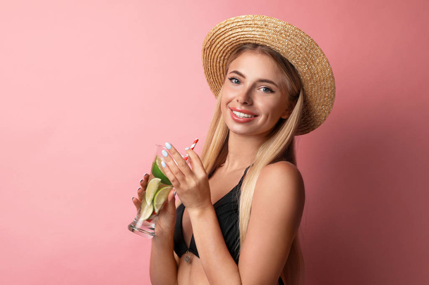 Pretty young woman wearing stylish bikini with cocktail on pink background - Foto, afbeelding