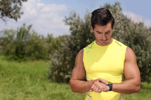 Young man checking pulse with smartwatch after training in park. Space for text - Foto, immagini