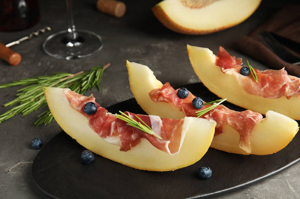 Melon with prosciutto, blueberries and rosemary on grey table - Foto, Bild