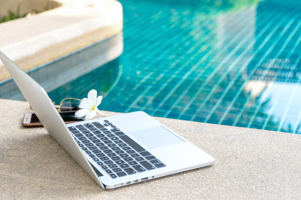 Laptop and smartphone near the swimming pool, modern businessman can work anywhere. - Foto, afbeelding