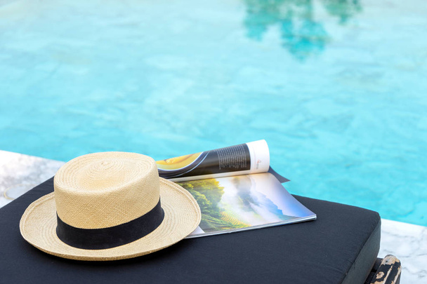 Kitap ve şapka yüzme havuzunun yanındaki güneş yatağında., - Fotoğraf, Görsel