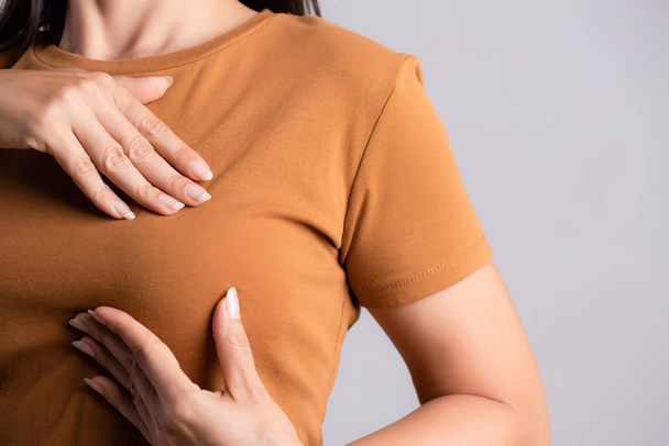 Frau überprüft Klumpen an ihrer Brust auf Anzeichen von Brustkrebs auf grauem Hintergrund. Gesundheitskonzept. - Foto, Bild