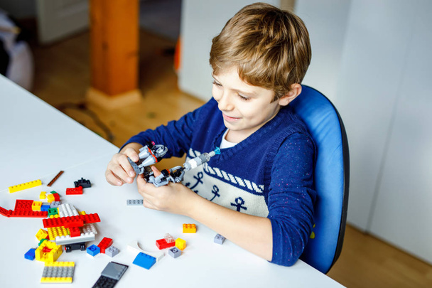 Little blond dziecko bawią się wiele kolorowych bloków plastikowych. Cute chłopiec szkoły Kid zabawy z budynku i tworzenia robota. Kreatywna rozrywka Nowoczesna technika i roboty. - Zdjęcie, obraz