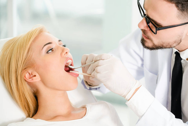 Joven dentista examinando paciente en clínica dental
. - Foto, Imagen