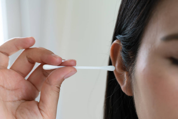 vrouw schoonmaken oor met wattenstaafje. Concept voor gezondheidszorg en oorreiniging - Foto, afbeelding