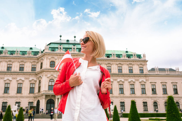 Female traveler with the flag of Austria against the backdrop of the Upper Belvedere Palace in Vienna. - Foto, afbeelding