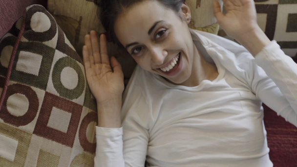 Portrait of happy smiling mixed race woman lying on couch at home at morning. Beautiful brunette female relaxing, stretches and yawns, laughing, enjoying morning time at weekend - Footage, Video