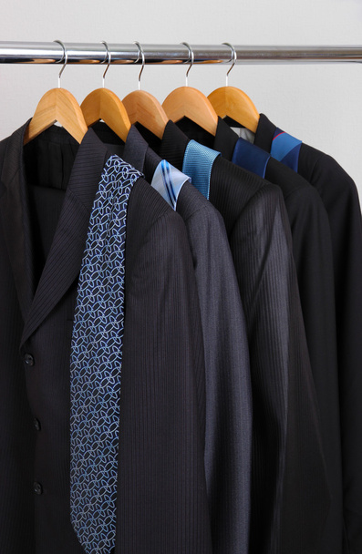 κοστούμια και γραβάτες στις κρεμάστρες σε γκρι φόντο - Φωτογραφία, εικόνα