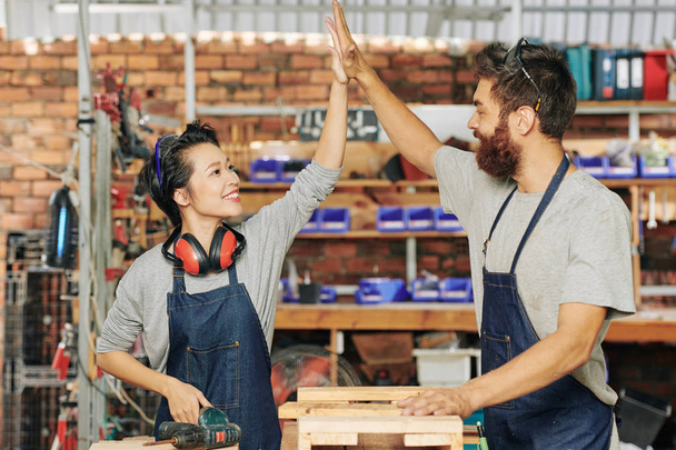 Happy young female carpenter giving high five to her coworker after finishing work - Photo, Image