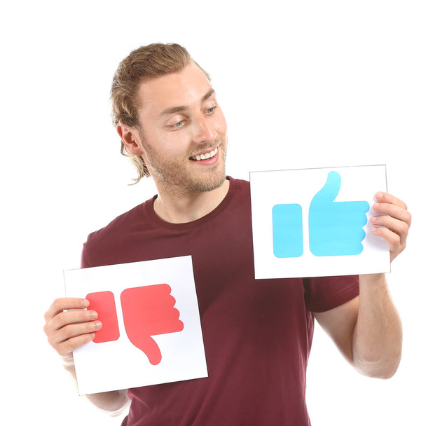 Male blogger holding papers with LIKE and DISLIKE signs on white background - Фото, зображення
