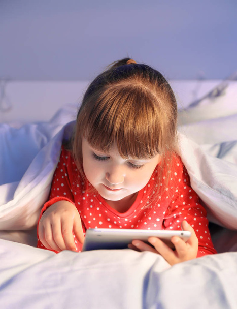 Linda niña usando tableta en la cama por la noche
 - Foto, imagen