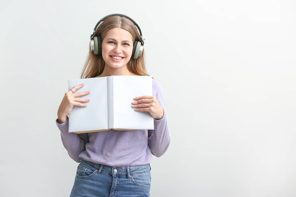 Mujer joven escuchando audiolibro sobre fondo blanco
 - Foto, Imagen