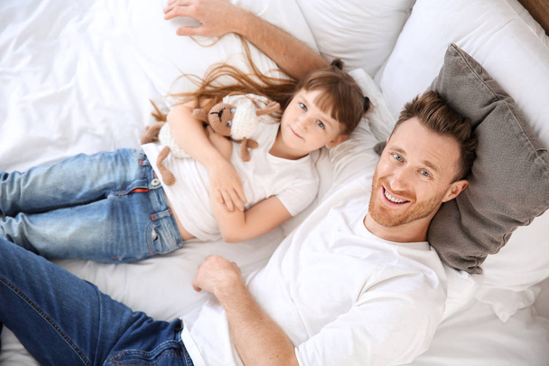 Portrait of happy father and his little daughter lying on bed, top view - Foto, imagen