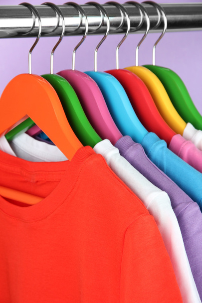 Different shirts on colorful hangers on purple background - Foto, Bild