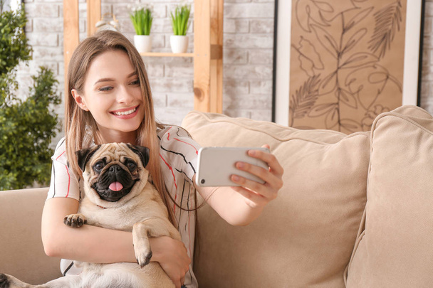 Gyönyörű fiatal nő aranyos mopsz kutyát vesz selfie otthon - Fotó, kép