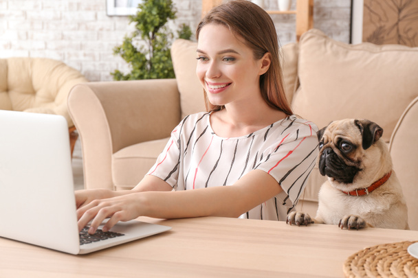 Mooie jonge vrouw met schattige Pug Dog werken op laptop thuis - Foto, afbeelding