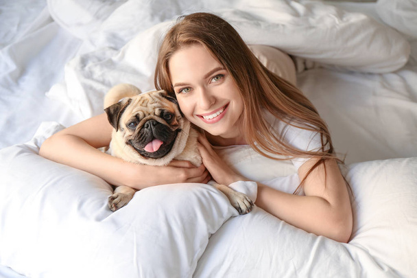 Rano pięknej młodej kobiety z cute pies Pug w sypialni - Zdjęcie, obraz