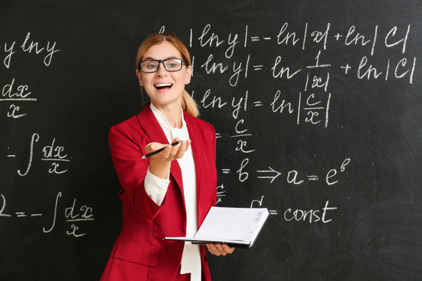Mooie wiskunde leraar met boek in de buurt van Blackboard in classroom - Foto, afbeelding