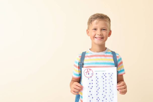 Счастливый мальчик с листом ответа на школьный тест на светлом фоне
 - Фото, изображение
