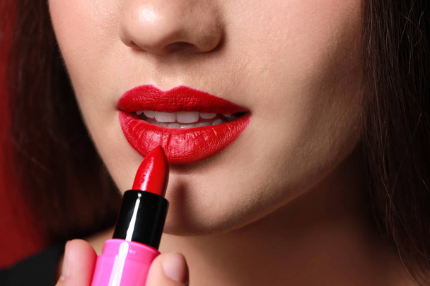 Beautiful young woman applying bright lipstick, closeup - Fotó, kép