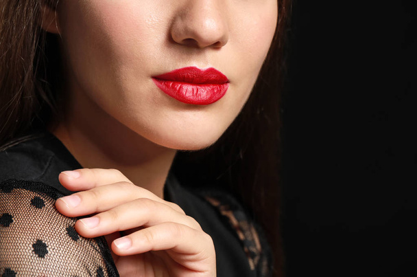 Beautiful young woman with bright lipstick on dark background, closeup - Photo, Image