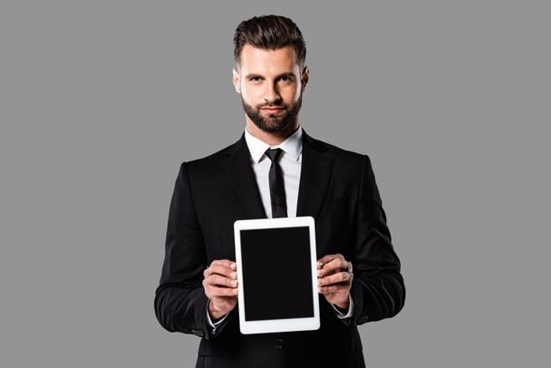 όμορφος επιχειρηματίας με μαύρο κοστούμι που δείχνει το ψηφιακό δισκίο με κενή οθόνη απομονώνεται σε γκρι - Φωτογραφία, εικόνα