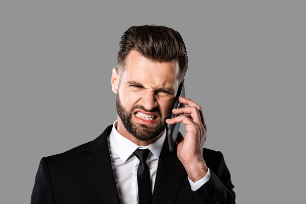 angry businessman in black suit talking on smartphone isolated on grey - Photo, image