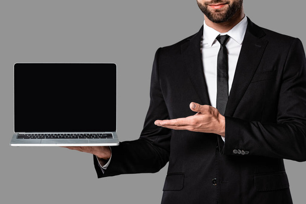 vue recadrée de l'homme d'affaires en costume noir pointant avec la main à l'ordinateur portable avec écran blanc isolé sur gris
 - Photo, image