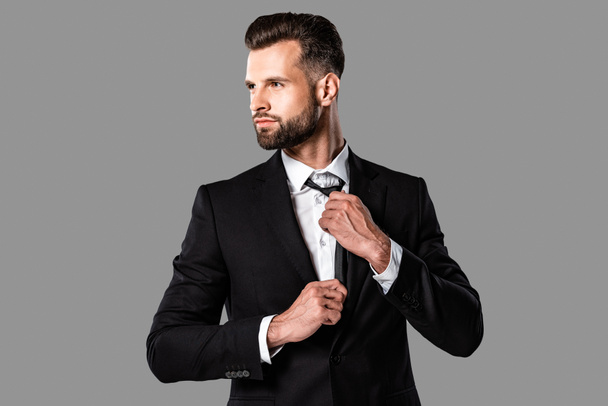 elegante hombre de negocios elegante en traje negro mirando hacia otro lado aislado en gris
 - Foto, imagen