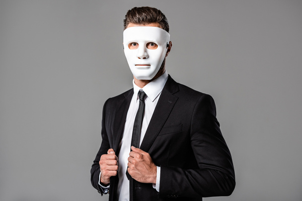 бизнесмен в черном костюме и белой маске изолирован на сером
 - Фото, изображение