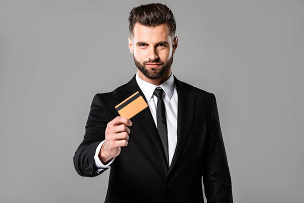 handsome businessman in black suit presenting credit card isolated on grey - Fotoğraf, Görsel