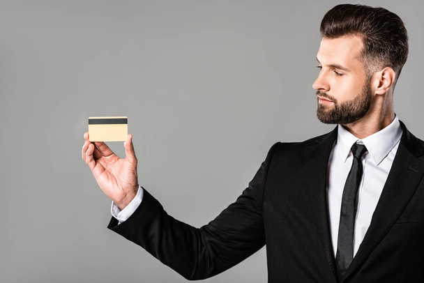 handsome businessman in black suit holding credit card isolated on grey - Foto, afbeelding